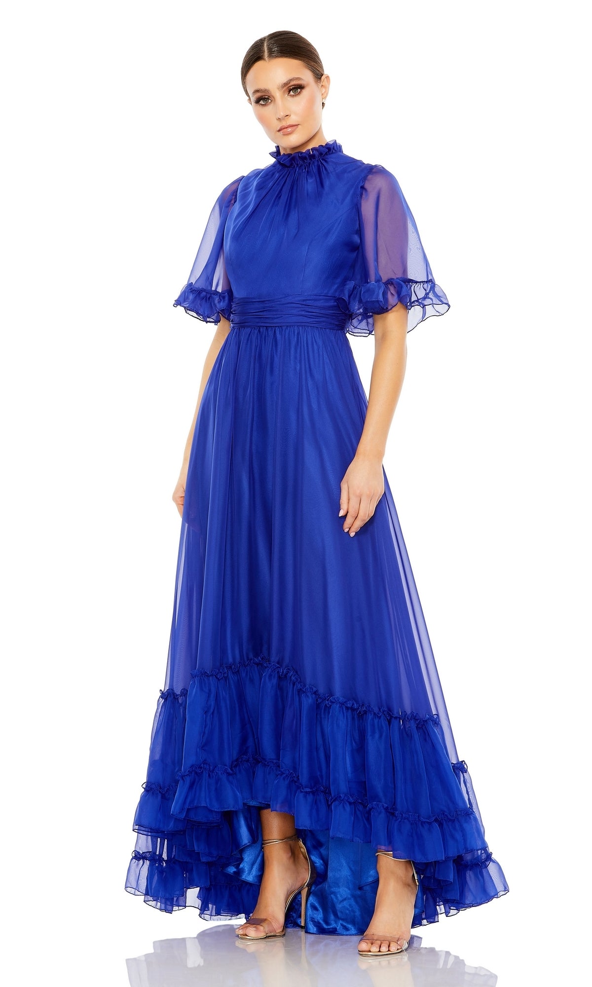 A woman stands against a white background wearing the Mac Duggal 68229, a royal blue short sleeve long formal dress featuring a high neck, ruffled hem, sheer sleeves, and an elegant a-line silhouette.